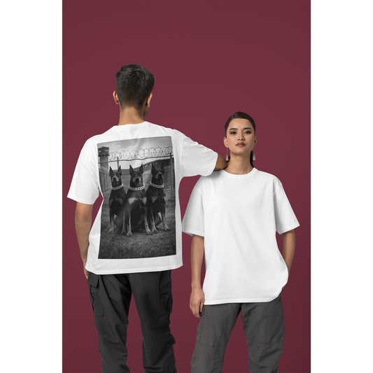 White unisex streetwear t-shirt worn by male model outdoors, back graphic featuring Doberman trio artwork, motivational fashion focused on discipline, dominance, and mental resilience