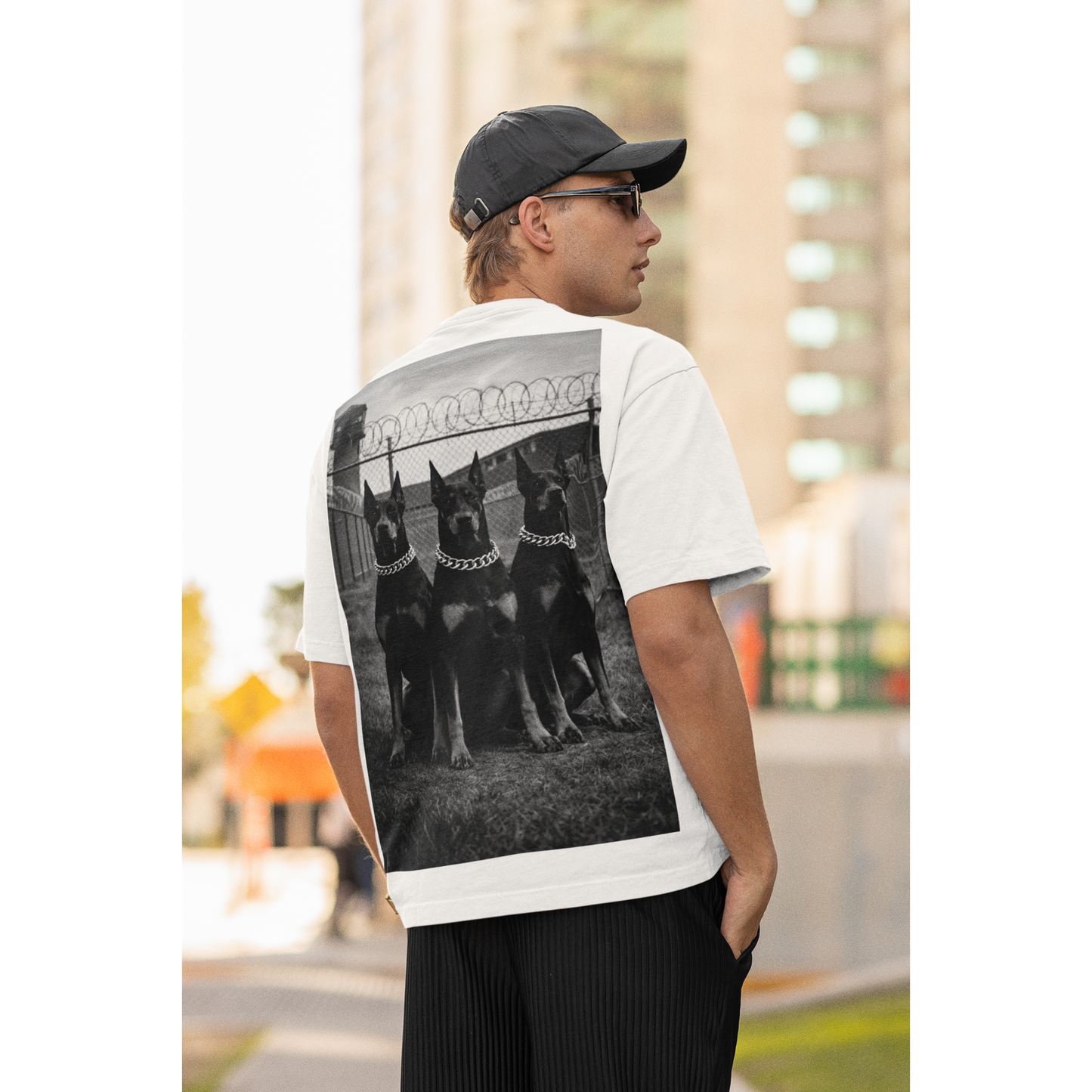 White unisex streetwear t-shirt worn by male model outdoors, back graphic featuring Doberman trio artwork, motivational fashion focused on discipline, dominance, and mental resilience