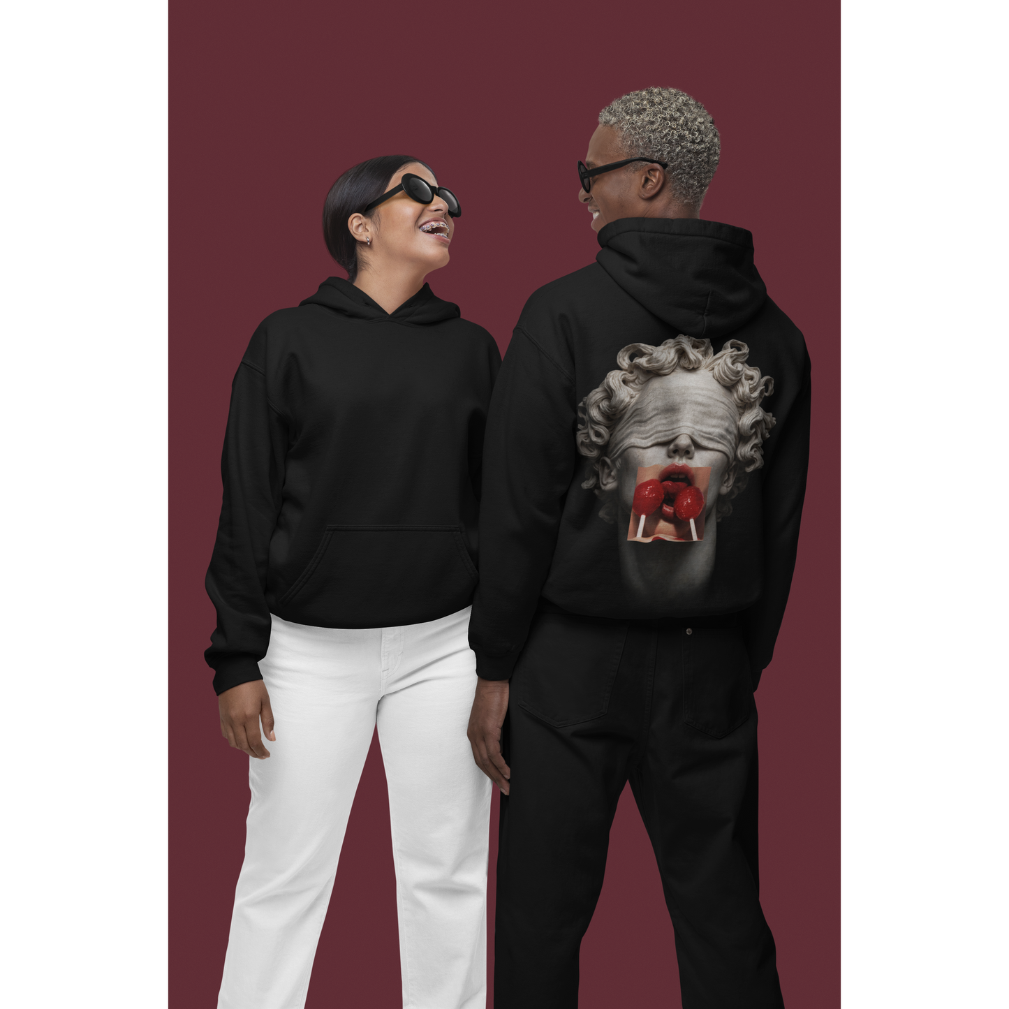 Two models wearing black hoodies with blindfolded classical statue back graphic, surreal marble sculpture with red lollipops, unisex streetwear