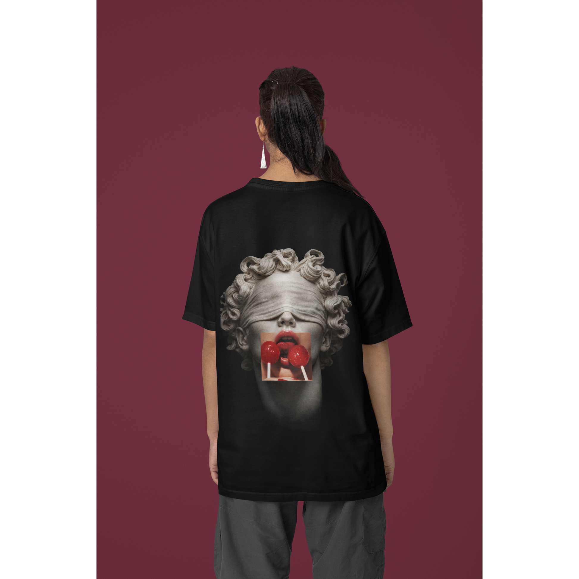 Black t-shirt worn in studio setting by female model, blindfolded classical statue back graphic with red lollipops, modern statement streetwear