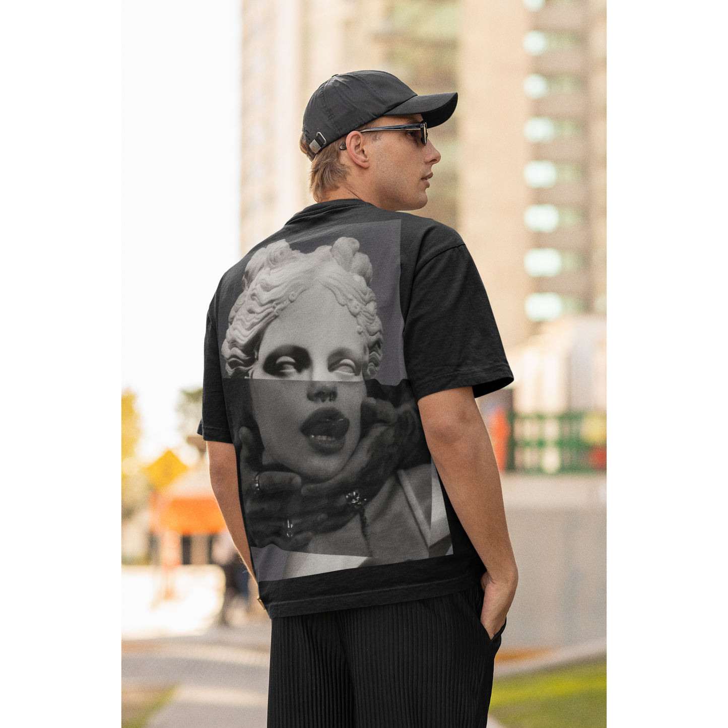 Male model wearing black surreal statue back graphic t-shirt outdoors, dark luxury streetwear tee featuring bold classical statue collage artwork on the back with clean minimalist front design