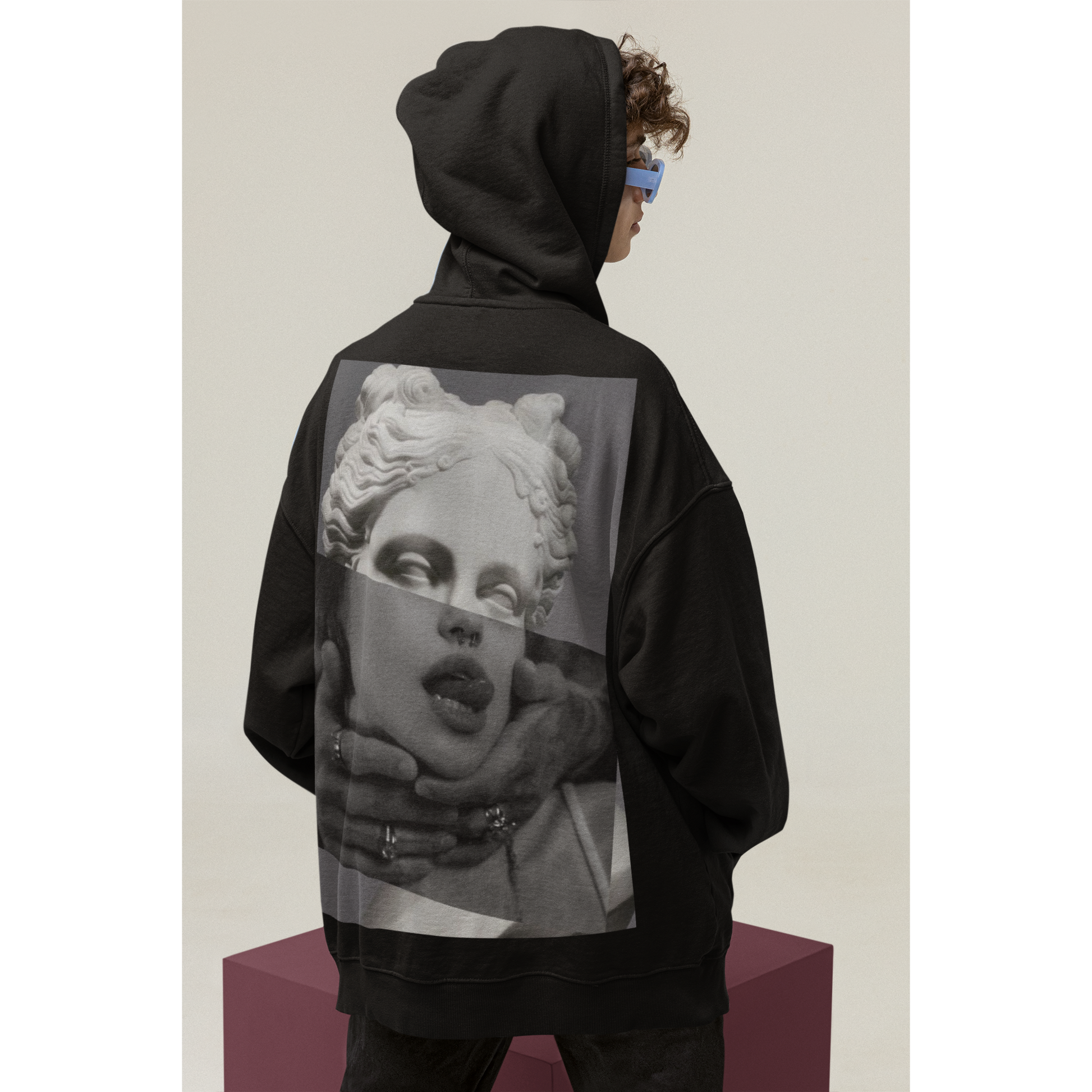 Black surreal statue back graphic hoodie shown in studio with hood up, unisex premium streetwear hoodie featuring surreal classical statue collage artwork printed on the back and clean front silhouette