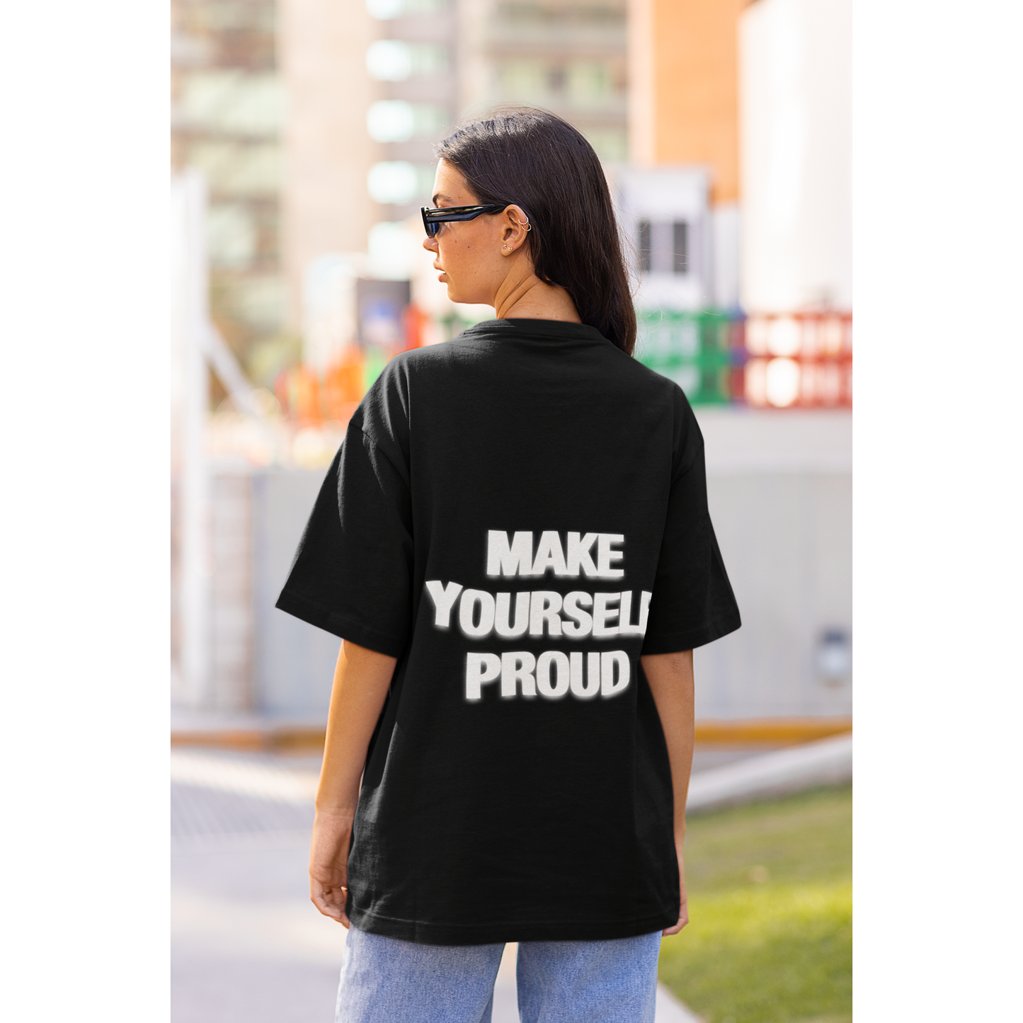 Person wearing a black t-shirt with 'MAKE YOURSELF PROUD' text on the back, standing outdoors. Unisex black statement t-shirt worn in modern streetwear style

