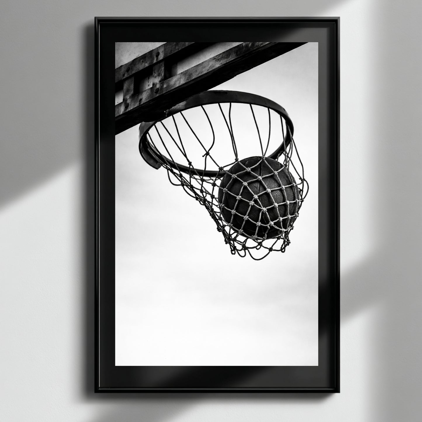 Minimal black and white basketball hoop wall art in black frame on neutral wall, modern sports photography print featuring suspended basketball