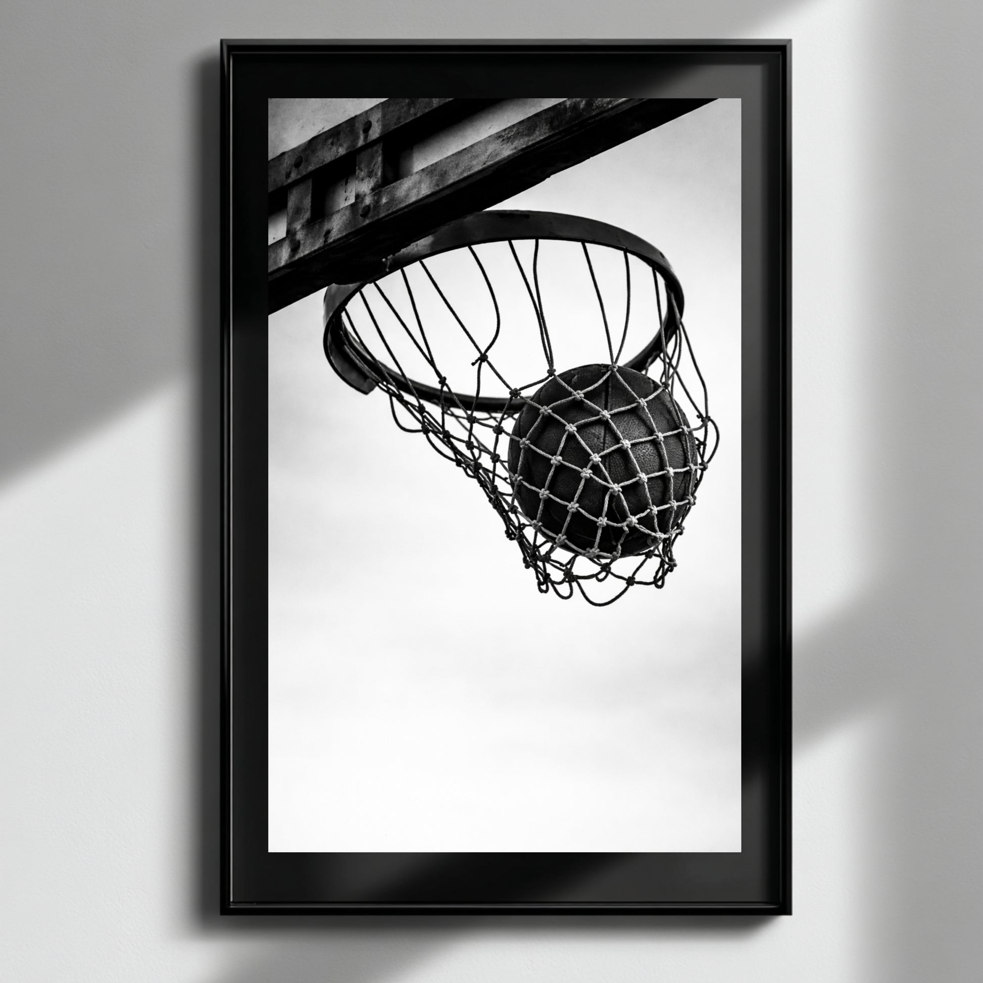 Minimal black and white basketball hoop wall art in black frame on neutral wall, modern sports photography print featuring suspended basketball