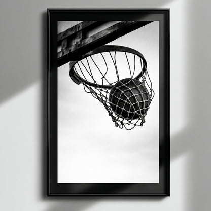 Minimal black and white basketball hoop wall art in black frame on neutral wall, modern sports photography print featuring suspended basketball