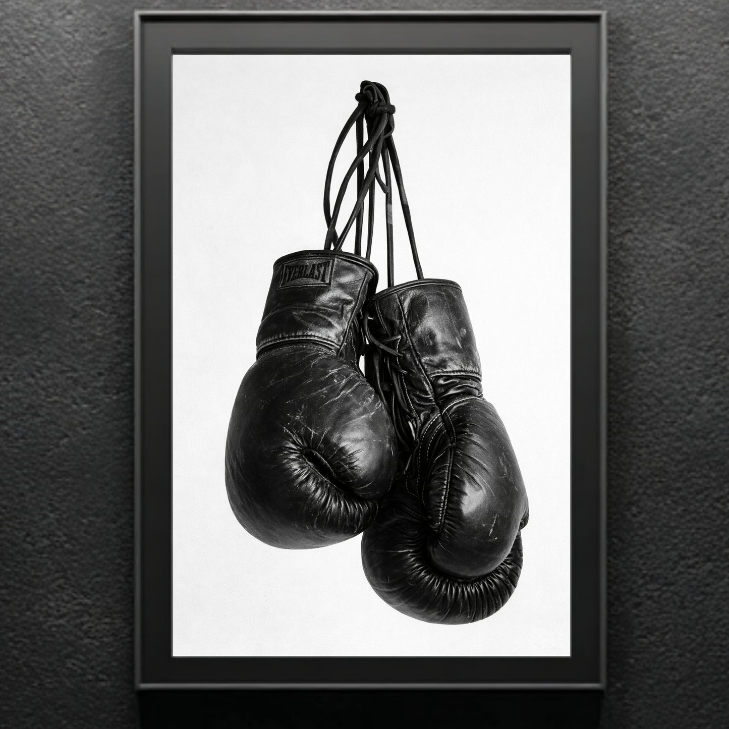 Black and white boxing gloves wall art in modern black frame against textured gray wall, vertical monochrome sports photography print for gym or office decor