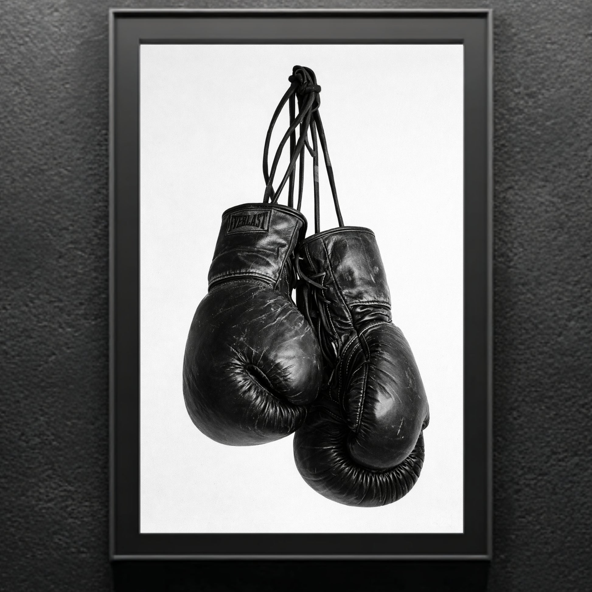 Black and white boxing gloves wall art in modern black frame against textured gray wall, vertical monochrome sports photography print for gym or office decor