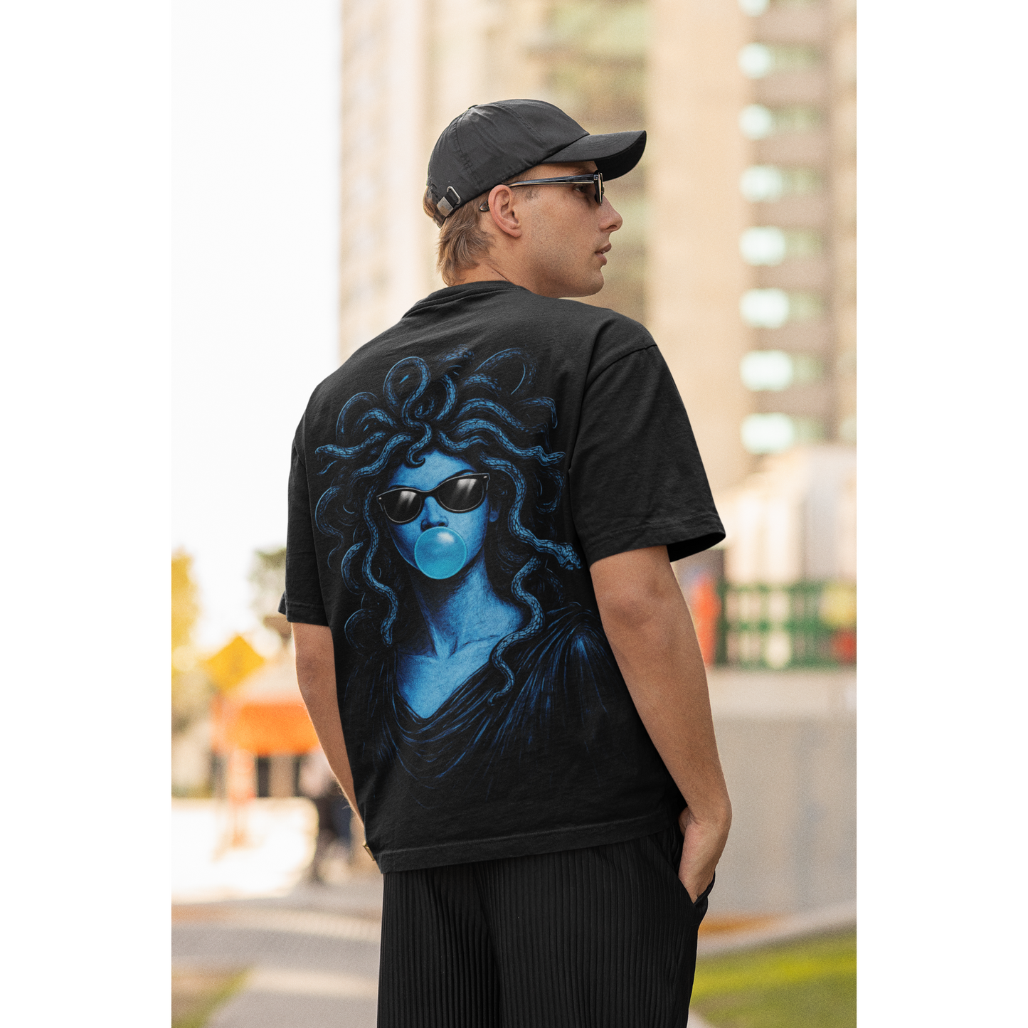 Male model wearing black blue medusa bubblegum back graphic t-shirt outdoors, unisex dark luxury streetwear tee featuring blue medusa figure with sunglasses blowing bubblegum and bold back graphic design